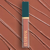 Lip gloss with teal cap and gold text on a brown swatch background