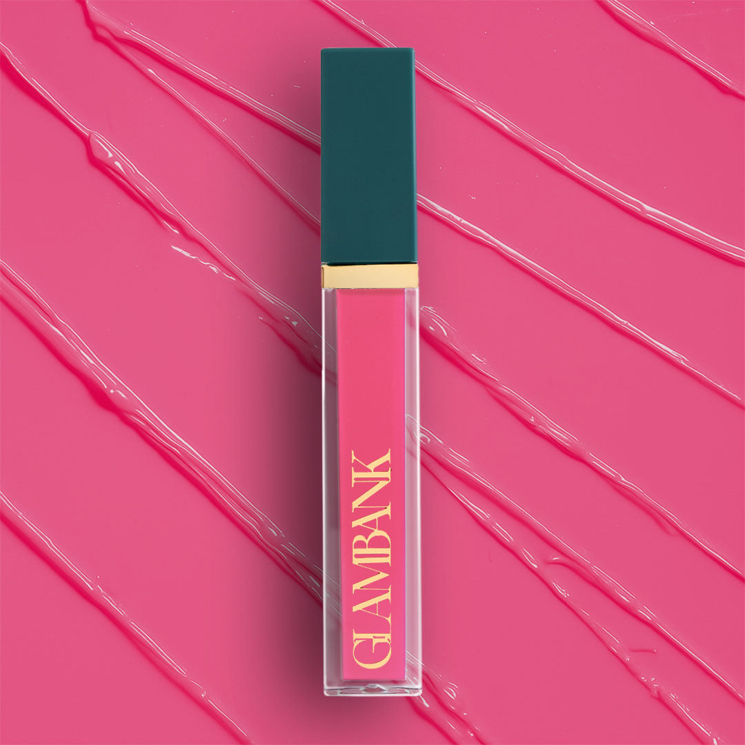 Lip gloss with teal cap and gold accents on a pink background